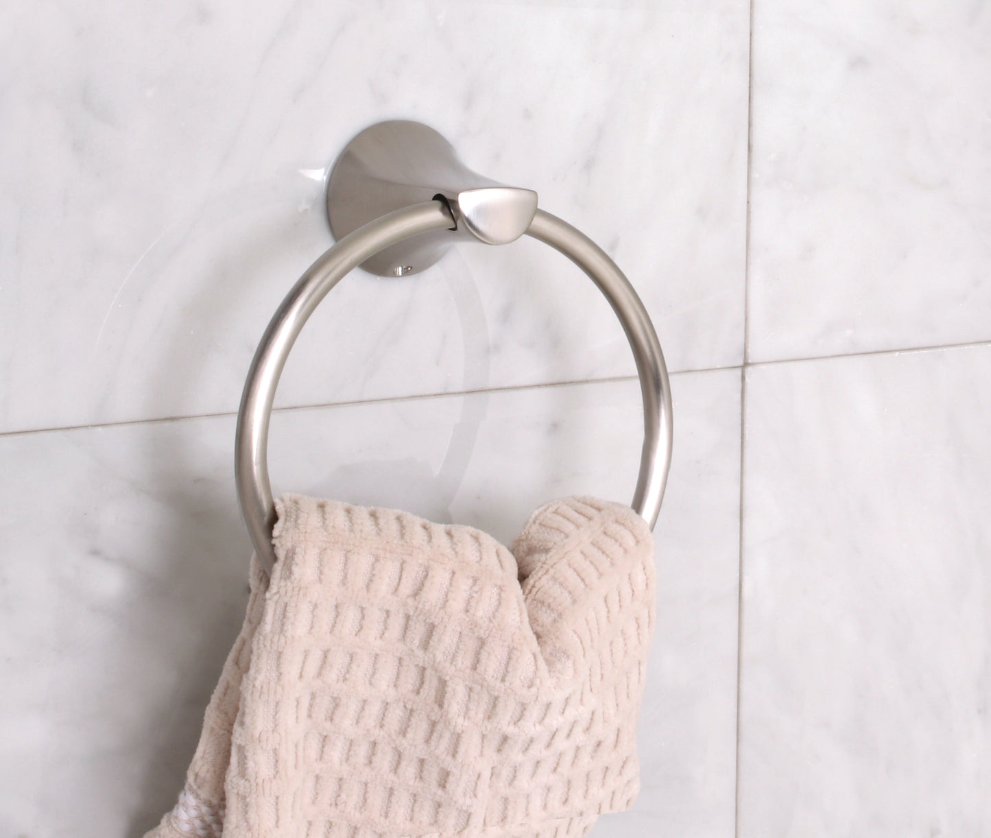 Metal towel ring with a beige towel on a tiled wall